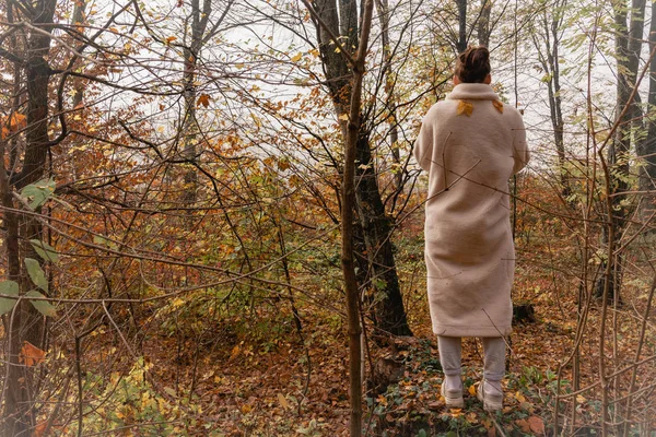 Jovem morena feminina de casaco branco fica de volta para a câmera entre a floresta colorida — Fotografia de Stock