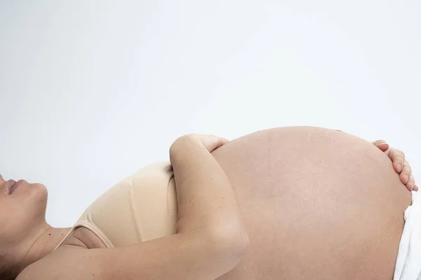 Gros plan de la femme enceinte couchée sur le sol et tenant ses mains sur son ventre gonflé, isolée sur fond blanc — Photo