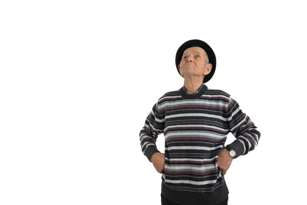 Pensive old man in casual clothes and black hat, thoughtful proud senior holds his hands on his waist, isolated over white background, copyspace for your text — Stock Photo, Image