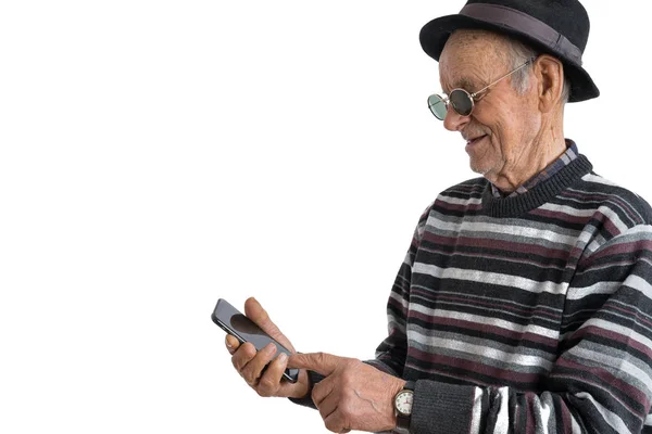 Handsome old man in casual clothes, black hat and sunglasses, senior looking attention at his smartphone to reading news, isolated over white background, copyspace — Stock Photo, Image