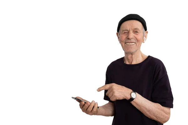 Красивый улыбающийся старик в черной футболке и шляпе, стильный старший в белых беспроводных наушниках, используя свой телефон и глядя на камеру изолированы на белом фоне, copyspace — стоковое фото