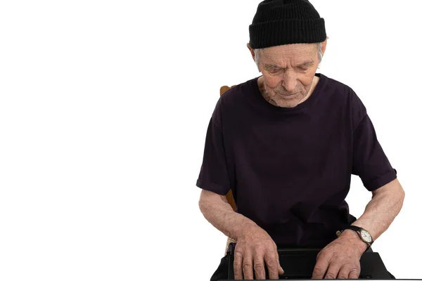 Confident old man in black hat and t-shirt sitting on chair, senior black hacker typing on the keyboard isolated over white background, copyspace — Stock Photo, Image