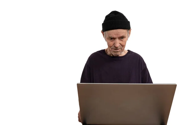 Closeup portrait senior, elderly, mature, man in black hat and t-shirt trying to figure out how use laptop internet isolated white background. Human emotion, facial expression. Age related changes — Stock Photo, Image