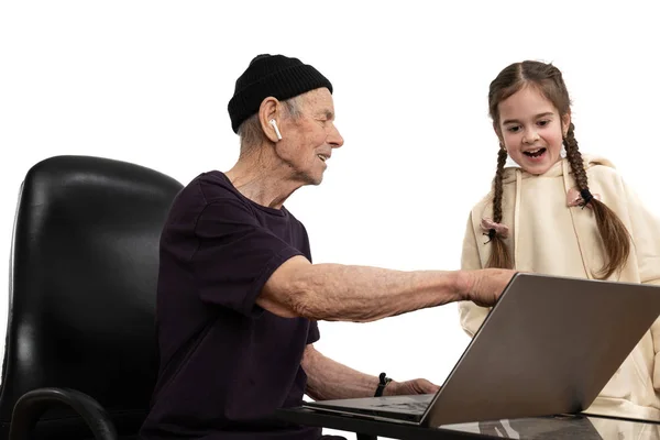 Stylish old man in black hat and t-shirt teaches his granddaughter programming by using laptop, isolated over white background — Stock Photo, Image