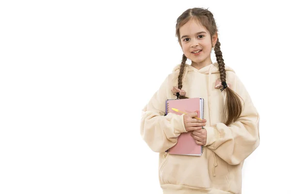 Vacker ung flicka student med flätor klädda i beige hoodie håller i händerna anteckningsbok och penna, tittar på kameran, isolerade över vit bakgrund, copyspace — Stockfoto