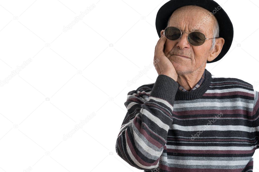 Stylish old man in casual clothes black hat and sunglasses holds his hand on his cheek wile has a toothache isolated over white background, copyspace for your text