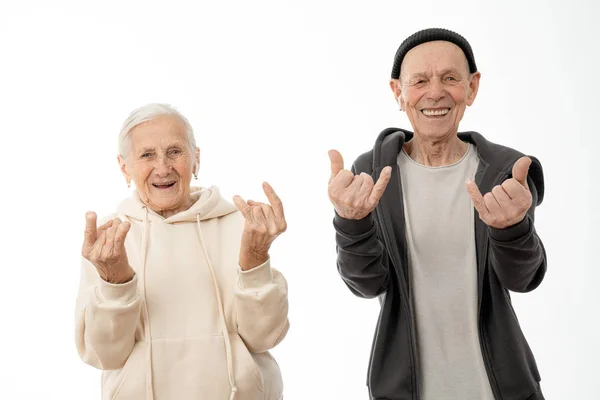 Atraente positivo idosos casal em capuzes, homem velho e mulher fazendo rock and roll gesto e olhando para a câmera isolada sobre fundo branco — Fotografia de Stock