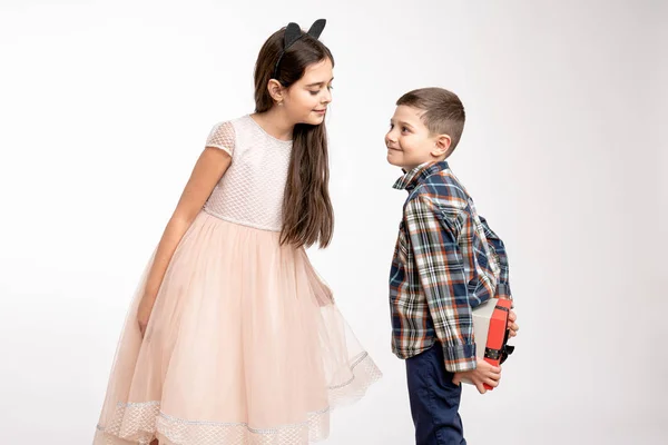 Attractive brunette girl in beige dress and with black ears on her head, sister waiting for a present, her brother in shirt holds a gift box in hands behinde his back. St. valentines day, Womans day — Stockfoto