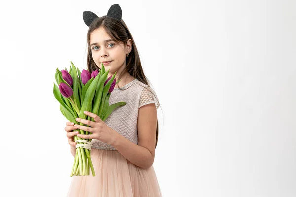 Confident, calmy brunette girl in beige dress holds purple flowers in her hands and looking at the camera isolated over white background, copyspace for your text — Stockfoto