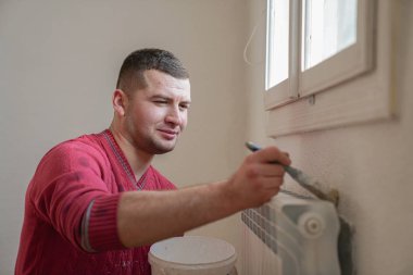 Construction worker and handyman doing finish renovation at apartment. Professional painter using paint roller brush painting of wall with white color on construction site.