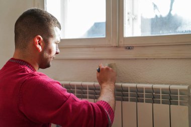 Portrait of painter young man in red t-shirt painting the wall in white color, with paint roller brush, home decor