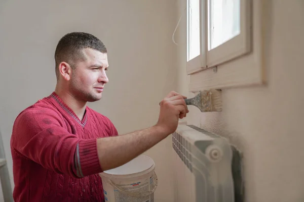 Construction worker and handyman doing finish renovation at apartment. Professional painter using paint roller brush painting of wall with white color on construction site.