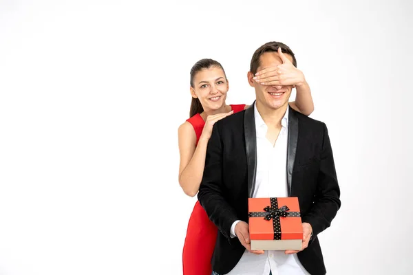 Regalo de San Valentín Pareja joven feliz en ropa elegante con regalo de San Valentín aislado sobre un fondo blanco. Chica morena feliz en vestido rojo dando un regalo a su novio en blaser negro — Foto de Stock