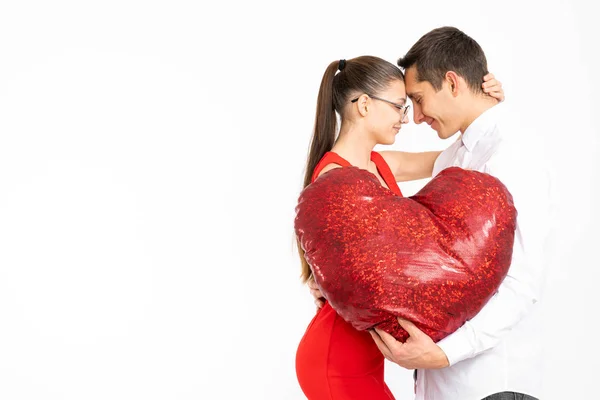 Hermosa pareja romántica aislada sobre fondo blanco. Atractiva joven mujer y hombre guapo están abrazando con los ojos cerrados mientras sostiene el corazón rojo en las manos. Feliz día de San Valentín Copyspace para — Foto de Stock