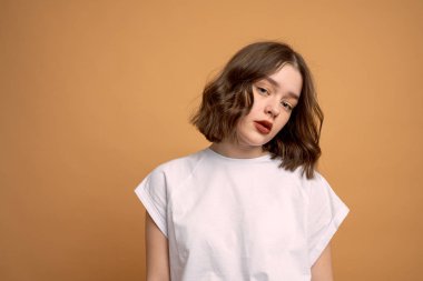 Beyaz tişörtlü, turuncu arka planda kameraya bakan kendine güvenen kıvırcık kız.