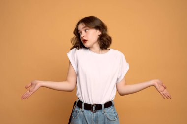 Kolları açık poz veren düşünceli, genç ve güzel bir esmer kadının portakal rengi arka planda sol tarafa baktığı görüntüsü..