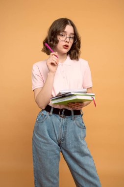 Gerçekten meşgul, ödev projesi, okula dönüş, turuncu arka planda gözlüklü kıvırcık öğrenci, yeni okul yılı, sınavlara hazırlanan kız. Okuldaki kız öğretmen..