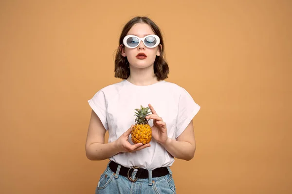 Fashionabla unga kvinnor i vita solglasögon håller ananas i händerna och tittar på kameran — Stockfoto
