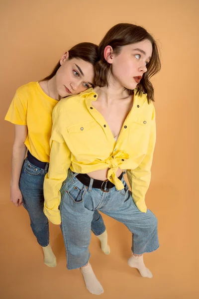 Upprörd, olycklig brunett flickor i gula skjortor står tillsammans isolerade över orange bakgrund — Stockfoto