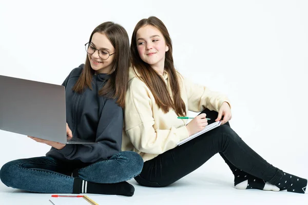 Två unga affärskvinnor i casual kläder sitter på marken med laptop och anteckningsbok, arbetar tillsammans på ett projekt — Stockfoto