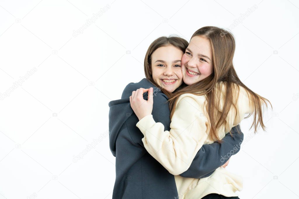 Ecstatic friends embracing on blue background. Studio shot of cheerful girls looking at camera, sisters hugging while spending time together isolated over white background