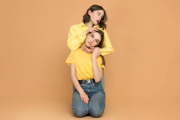 Cousins in chic summer cotton yellow shirts are chatting nicely. Young women posing on light orange background — Stockfoto