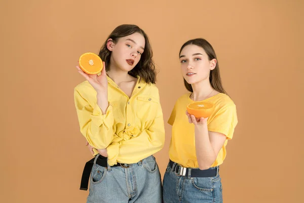 Dos chicas morenas deportivas con ropa casual. Mujer con frutas aisladas sobre fondo naranja —  Fotos de Stock