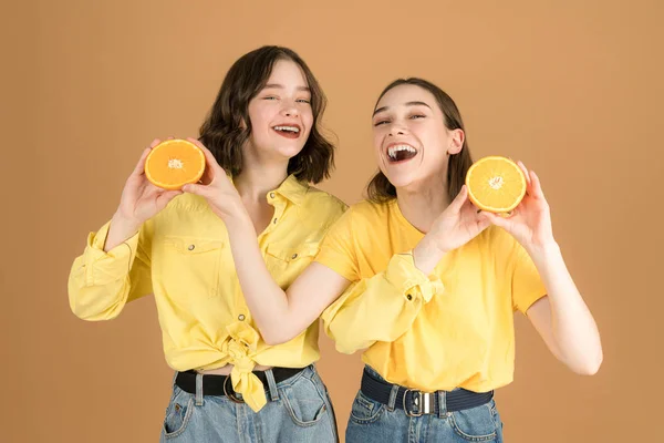 Feliz morena hermanas vegetarianas con rodajas de naranja en las manos sonriendo y mirando a la cámara —  Fotos de Stock