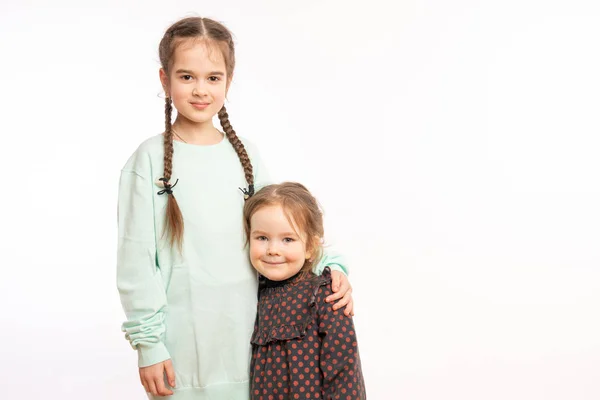 Horizontal shot of small girl embraces older sister with love, missed her very much, wants to play together, glad to have each other, look alike, have truthful friendship. — ストック写真