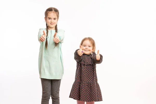 To søte barn som står over isolerte hvite bakgrunnstegn som gjør positive gester med hånden, tomler opp smilende og glade. Munter og vinnergester . – stockfoto