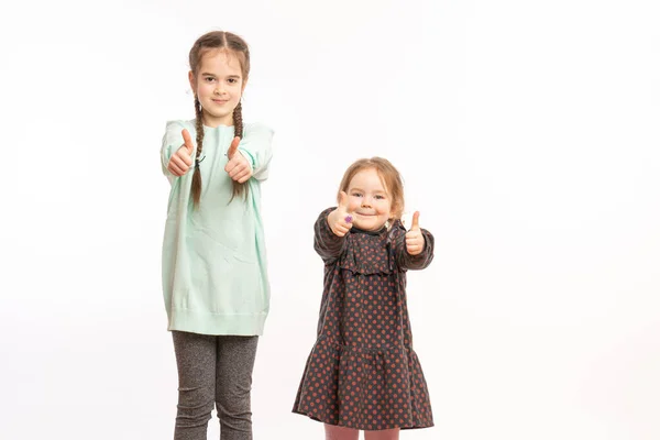 Two cute children standing over isolated white background success sign doing positive gesture with hand, thumbs up smiling and happy. Cheerful expression and winner gesture. — Stockfoto