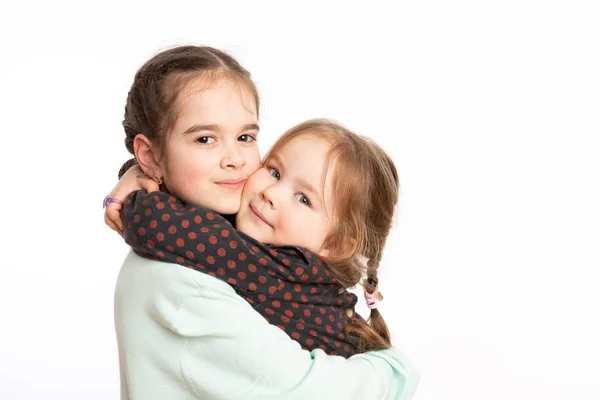 Waist up portrait of two little sisters hugging and looking at the camera isolated over white background with copyspace — Stockfoto