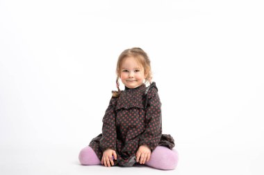 Pretty little girl with red hair and pigtalis dressed in purple tights sitting on the floor and looking at the camera