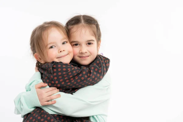 Lovely sisters in casual clothes hugging each other and looking at the camera, happy family concept, isolated portrait — Stock Photo, Image