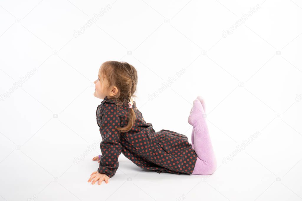 Little playfull girl in dress lying on the floor looking to the copy space area, isolated over white background