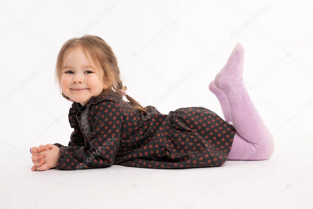 Happy adorable redhead little girl in dress smiling and looking at the camera while liying on the ground