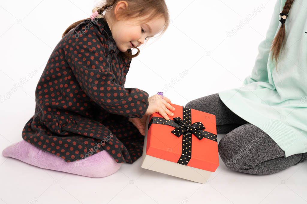 Two girls sitting on the floor, little child in purple tights opened present box from her sister, Merry Christmas concept