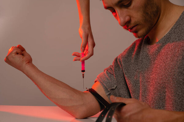 Junkie sloppy man waiting for the dose of heroine, females hand holds syringe above his hand