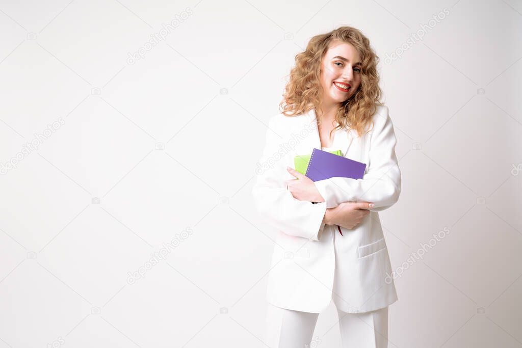 Beautiful business woman in white blazer holds notebooks in her hands and looking at the camera, isolated over white background