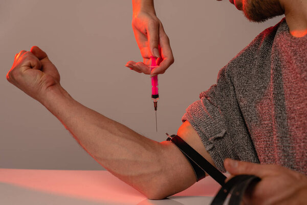 Males hand of a drug addict and females hand with narcotic syringe, studio photo with red light