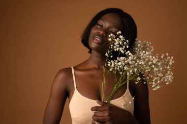 Feeling the spring. Gorgeous young African female smiling excitedly with her eyes closed holding a bunch of white flowers copyspace on the side