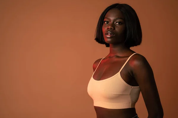 Waist up portrait of a young beautiful african girl in beige bra isolated over dark orange background — 图库照片