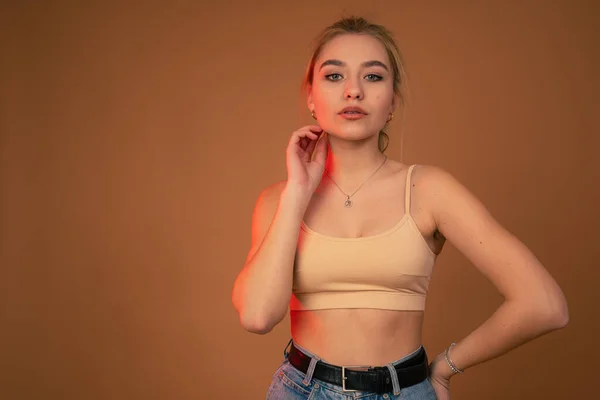 Waist up beauty portrait of a blonde girl with healthy natural skin dressed in beige bra looking at the camera isolated over dark orange background — ストック写真