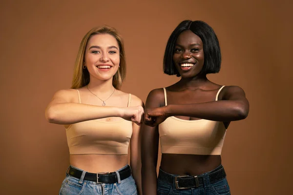 Image of two young teenage international girls smiling and bumping their fists together and looking at the camera isolated over dark orange background — Stockfoto