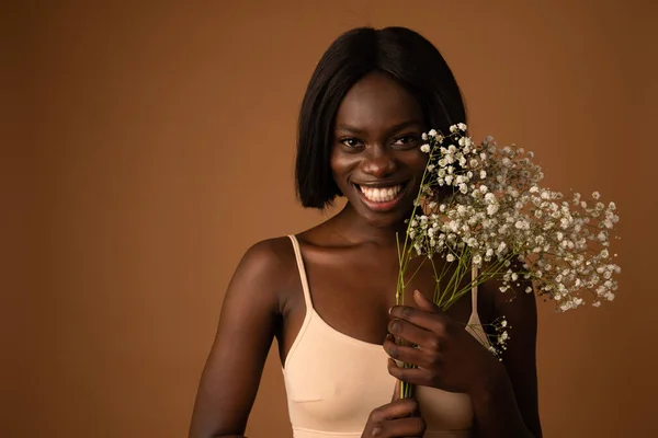 Happy african woman holding bouquet of white flowers and looking at the camera over yellow background — 图库照片