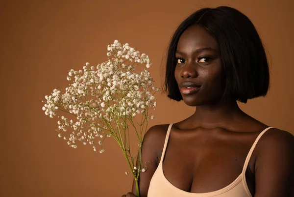 Attractive confident young black woman holding in hands fresh white flowers and looking at the camera isolated on orange background — 图库照片