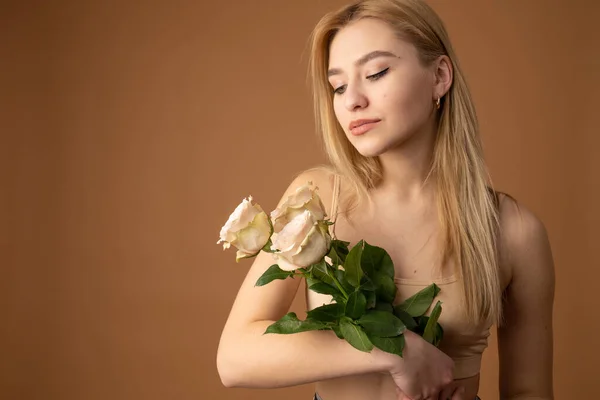 Beautiful blonde woman with clean fresh skin holding flowers and looking down, isolated over orange background — Φωτογραφία Αρχείου