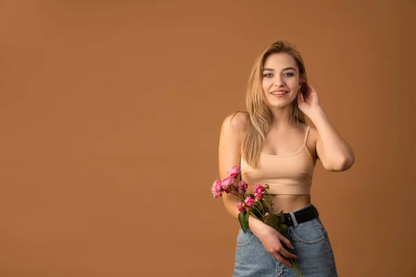 Sensual young blonde girl in beige bra holds pink flowers and looking at the camera isolated over orange background — Φωτογραφία Αρχείου
