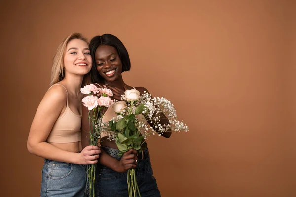 Funny young lesbian couple two international girls in casual outfit celebrating isolated on pastel orange background. Valentines Day Womens Day birthday holiday concept. Holding bouquet of flowers — Stockfoto