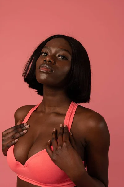 一个穿着粉色胸罩的性感非洲裔美国女孩的近照，她看着被粉色背景隔离的相机 — 图库照片